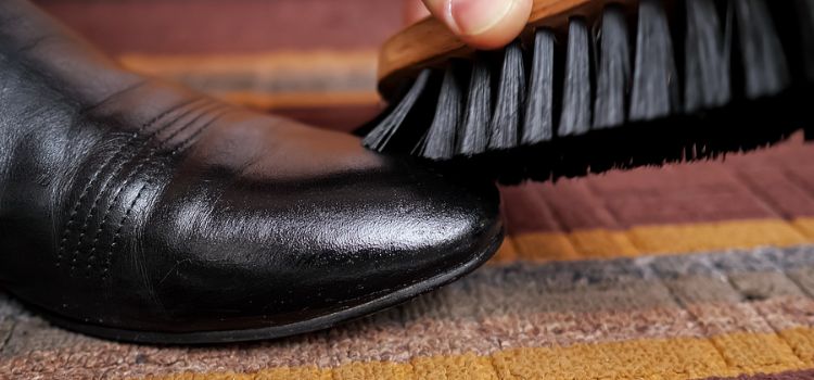 person cleaning leather boots with a brush.