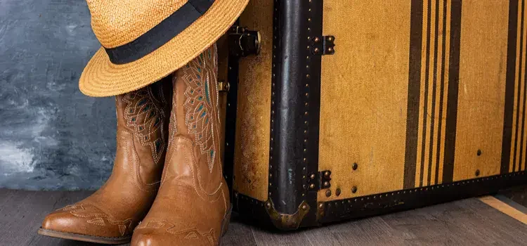 Pair of cowboy boots sitting next to a suitcase.