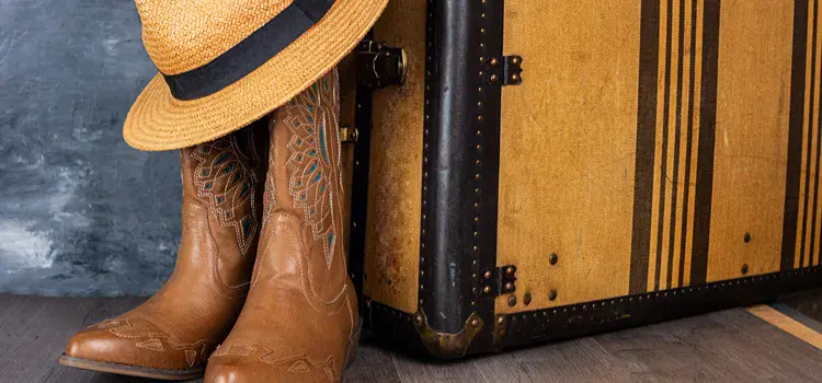 Pair of cowboy boots sitting next to a suitcase.